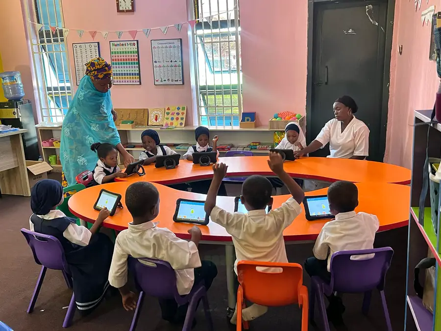 Nursery pupils raising their hands around a table of tablets