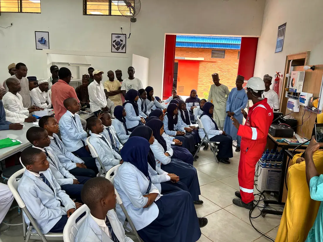 An engineer in red safety overalls explaining equipment to seated pupils