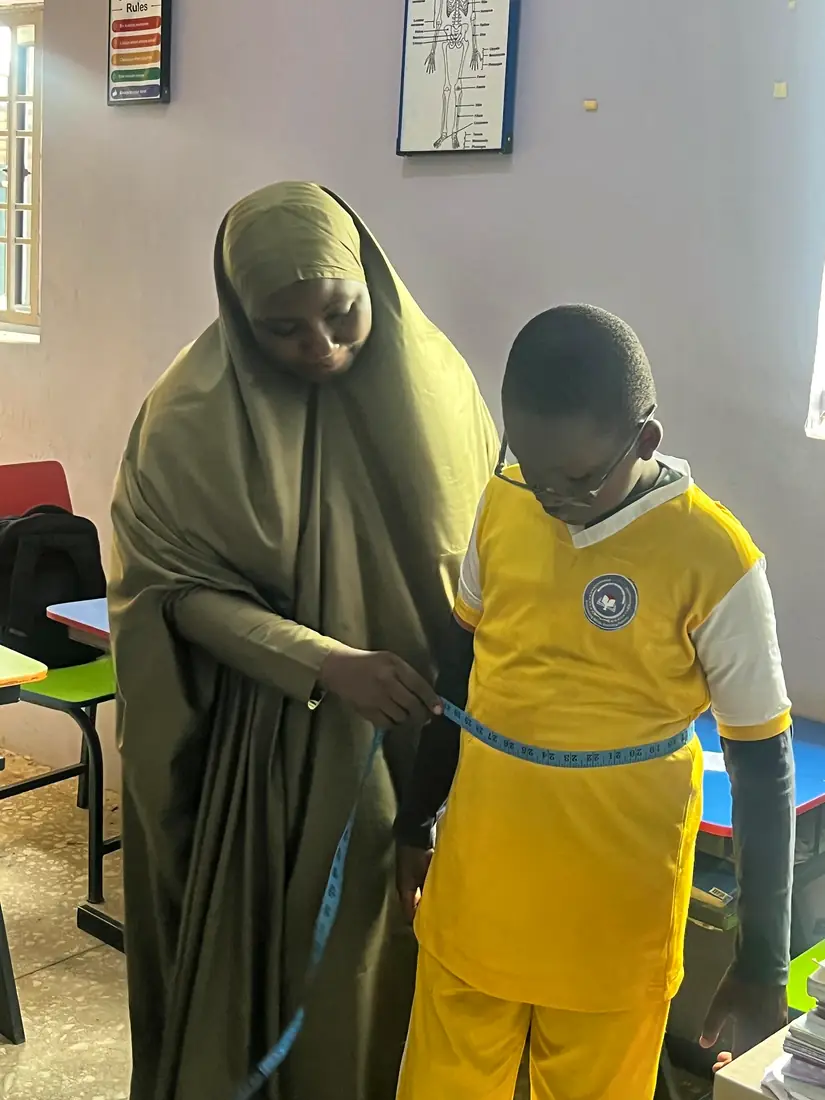 A teacher measuring a pupil with a tape measure