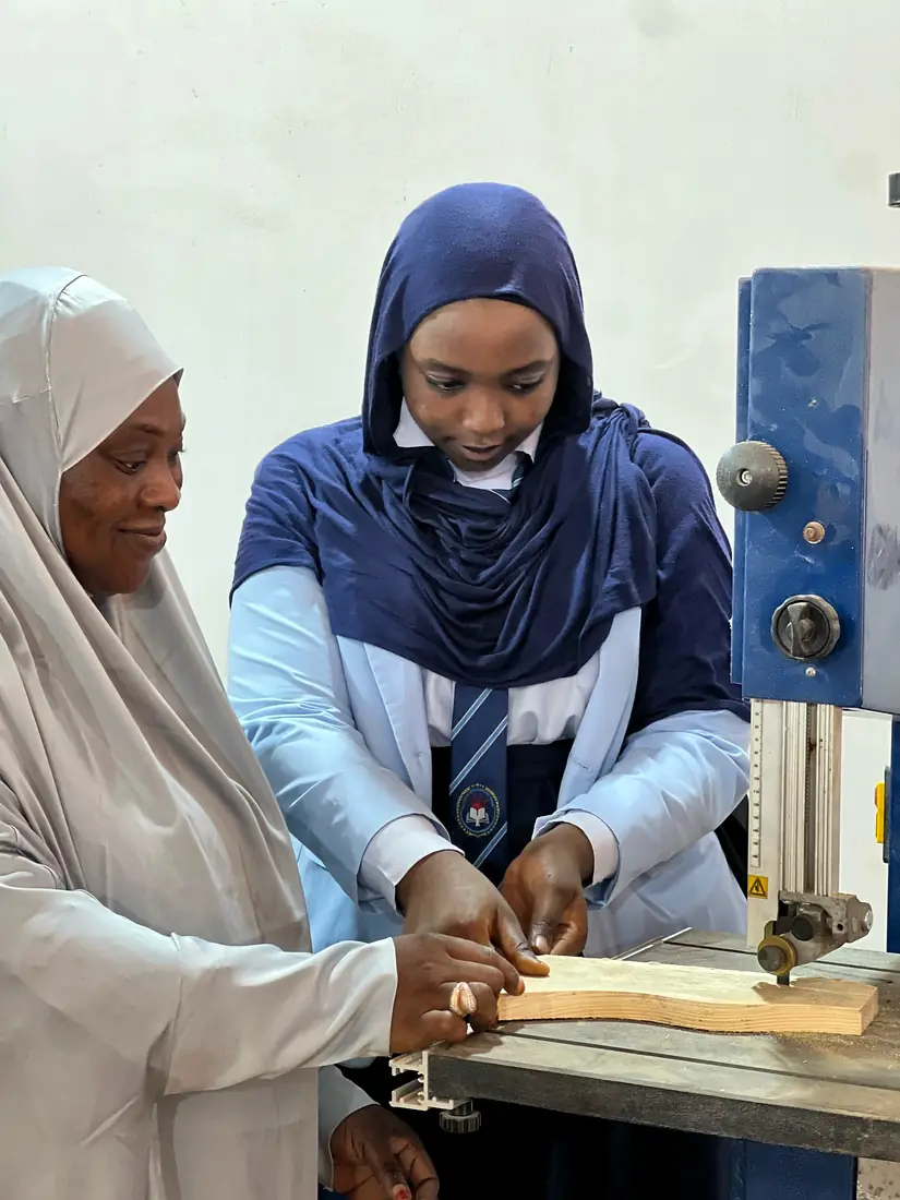 A pupil cutting wood on a band saw with a teacher